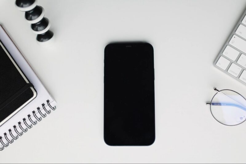 prikaz android telefona na stolu sa notesom, sveskom, tastaturom od kompa i naočarama